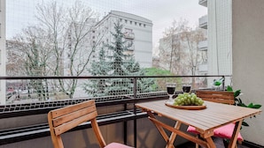 En balkon med et træbord og stole, en skål med grønne druer og et glas vin.