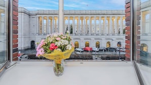 Et vindue med en blomsterbuket og udsigt til en klassisk bygning med søjler.