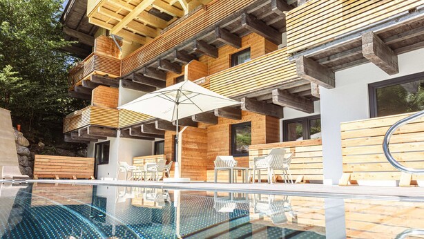 A modern outdoor pool area with wooden deck and lounge chairs. - Apartment in Saalbach Near ski Area (Saalbach-Hinterglemm)