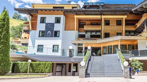 A modern hotel with a multi-story structure, a prominent entrance with steps, and a sign indicating it is a resort. - Exclusive Suite in the ski Area (Saalbach-Hinterglemm)