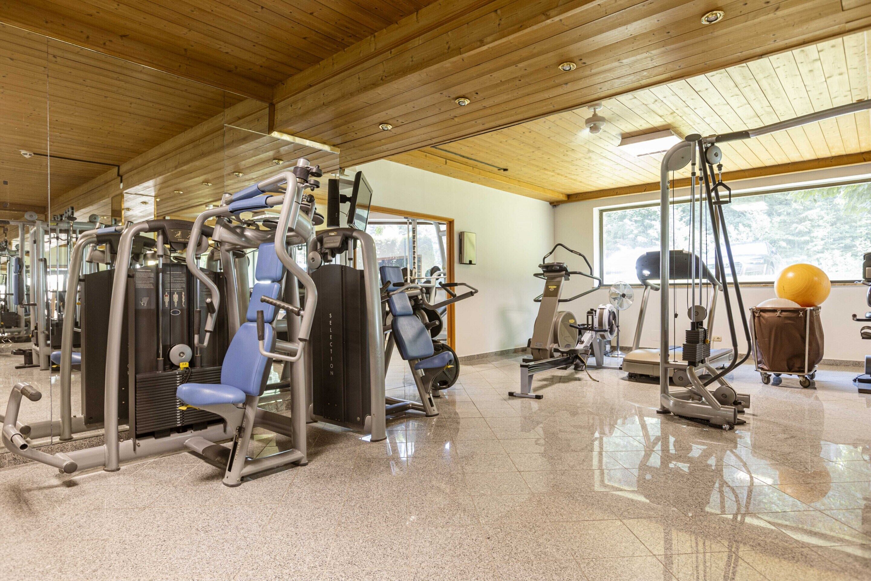 A gym with various exercise machines, a large mirror, and a window providing natural light.