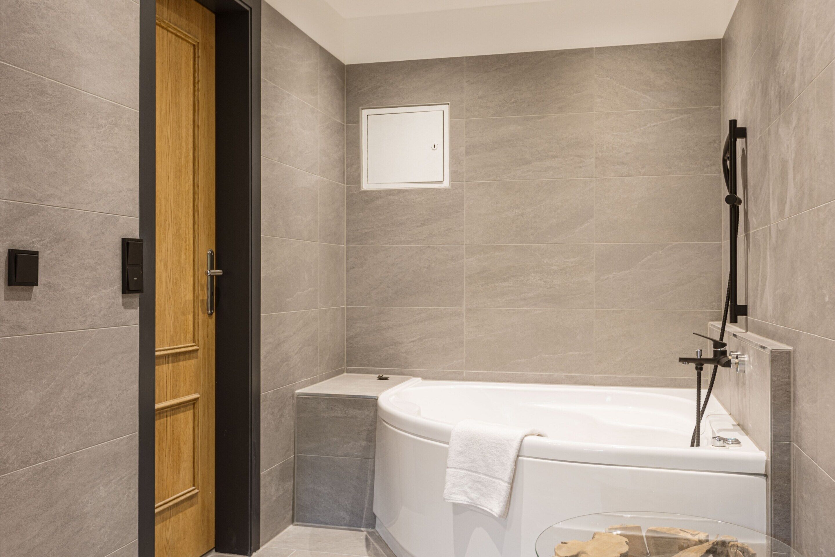 Un baño moderno con bañera, una puerta de madera y un estante pequeño.