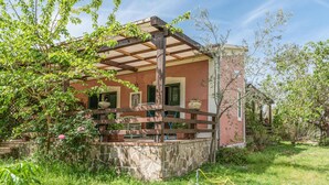 Een rustiek huis met een houten pergola, stenen fundering en weelderige begroeiing.