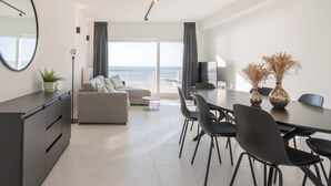 Uma sala de estar moderna com sofá, mesa de jantar, cadeiras e vista para o mar.