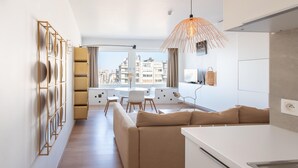 Una sala moderna con un sofá, una mesa de comedor y sillas. Hay una zona de cocina con una encimera blanca y una lámpara colgante.