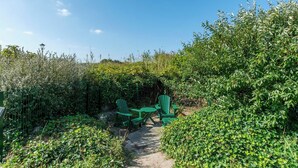Ein Gartenbereich mit einem gepflasterten Weg, grünen Stühlen und einem Tisch.