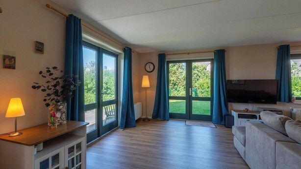 Ein geräumiges Wohnzimmer mit großem Fenster, einer Couch, einem Fernseher und einer Lampe auf einem Holztisch.