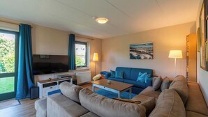 Ein Wohnzimmer mit einer Couch, einem Couchtisch, einem Fernseher und einem Fenster mit Vorhängen.