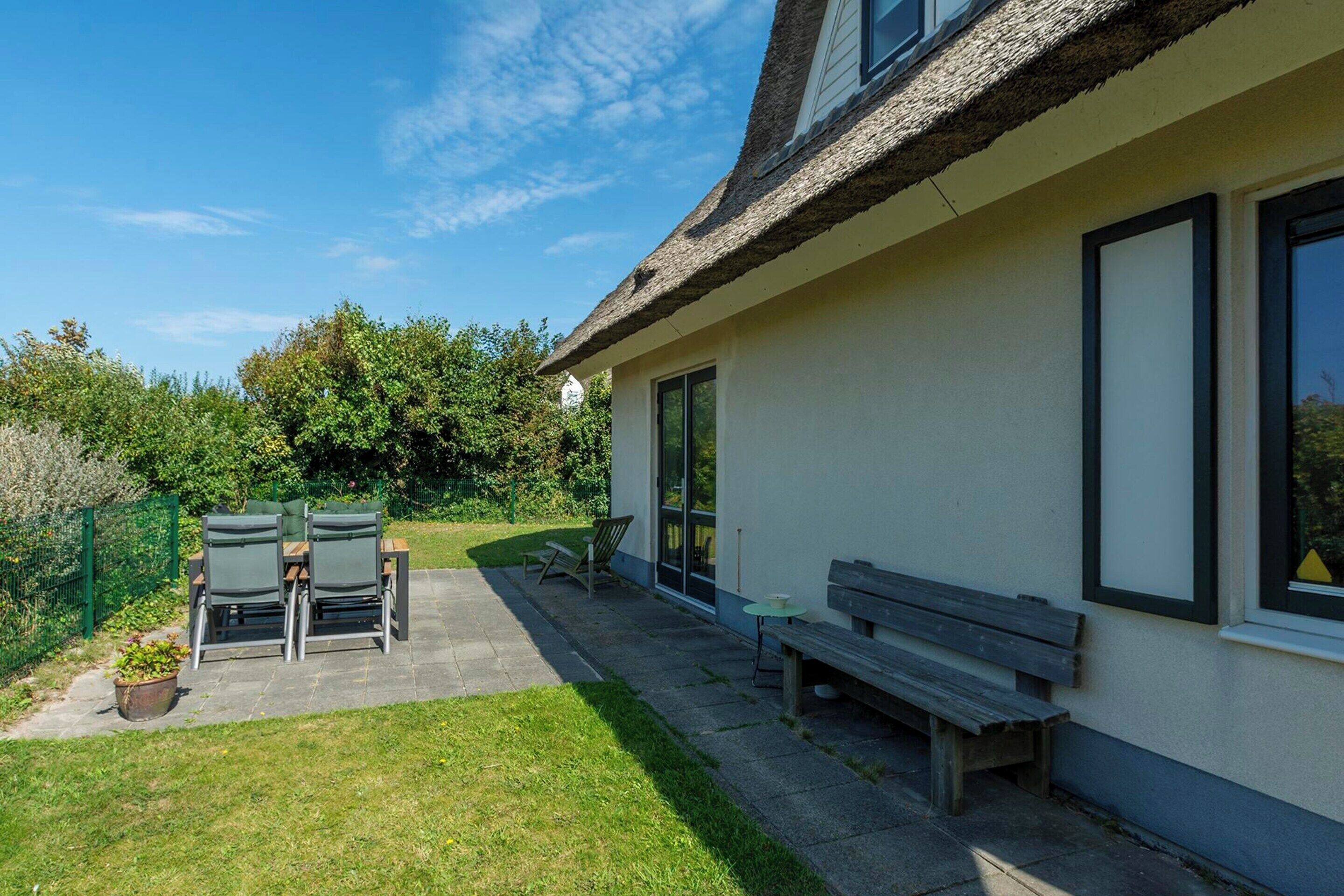A house with a patio area featuring a table and chairs, a bench, and a thatched roof.