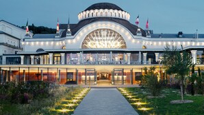 Imponente entrada de hotel con un gran ventanal arqueado y una cúpula central, rodeada de un camino bien iluminado y vegetación.
