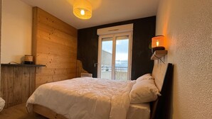 Un dormitorio con una cama de madera, una lámpara de pared y vistas a través de una puerta.