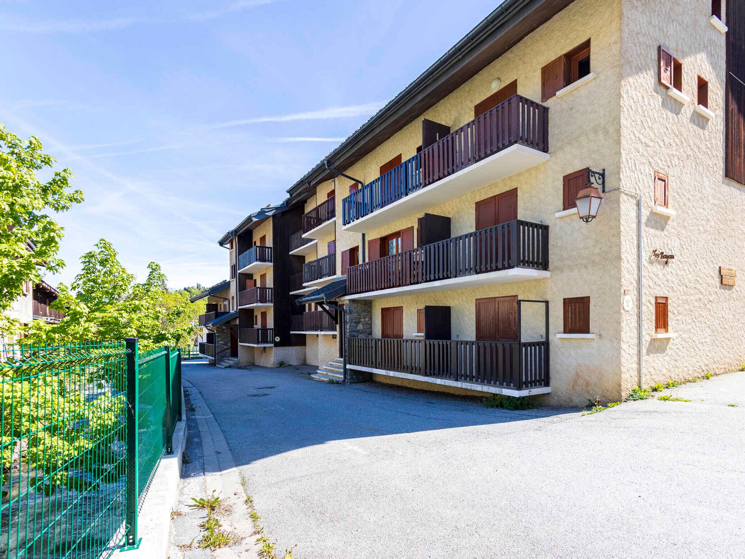 A multi-story building with balconies, a green fence, and a clear sky.
