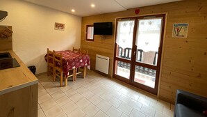 A cozy room with a wooden interior, a dining table with chairs, a TV mounted on the wall, and a window with frosted glass.