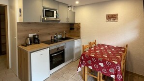 A compact kitchen with a microwave, stove, and sink. There is a small refrigerator and a table with a heart-patterned tablecloth.