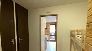 A hallway with a wooden door, a wooden bench, and a view into a room with a balcony.