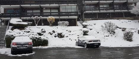 A building with a flat roof and large windows, surrounded by snow-covered ground and parked cars.