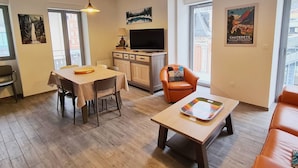 Una sala moderna con comedor, un sillón de cuero, televisor y ventana grande.