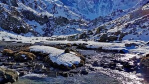 Paisaje montañoso con picos nevados y un arroyo cristalino.