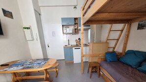 A compact room with a bunk bed, a small kitchenette, a dining table with chairs, and a sofa.