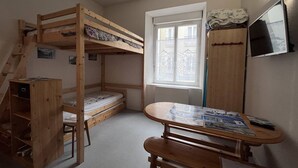 A bunk bed room with a desk and chair, a small cabinet, and a window.