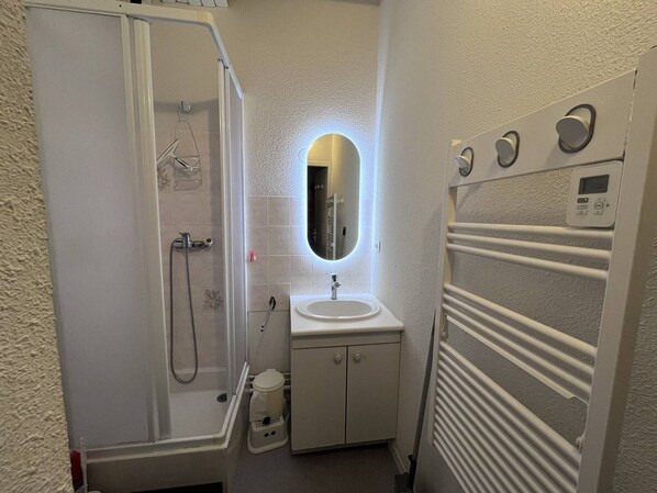 A bathroom with a shower, sink, mirror, towel rack, and a control panel.