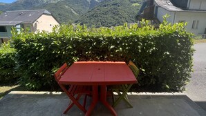 A red table and chairs set outdoors with a view of mountains and a hedge in the foreground. - Renovated apartment with terrace and parking in Cauterets (Cauterets)