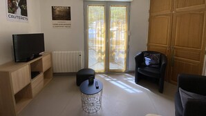 A living room with a TV on a wooden cabinet, a round table with a remote, a black chair, and a wardrobe. - Cozy apartment Cauterets, cable car, parking, Wi-Fi, 4 people (Cauterets)