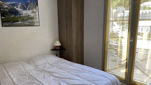 A bedroom with a bed, a lamp on a side table, a window with a view of buildings, and a painting on the wall. - Cozy apartment Cauterets, cable car, parking, Wi-Fi, 4 people (Cauterets)