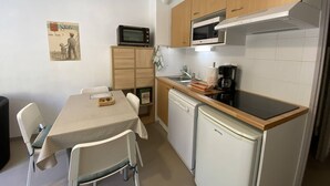 A compact kitchen with a microwave, stove, and refrigerator. There is a small dining table with chairs and a poster on the wall. - Cozy apartment Cauterets, cable car, parking, Wi-Fi, 4 people (Cauterets)