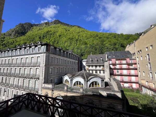 A historic building with classical architecture, a prominent balcony, and a mountain backdrop.