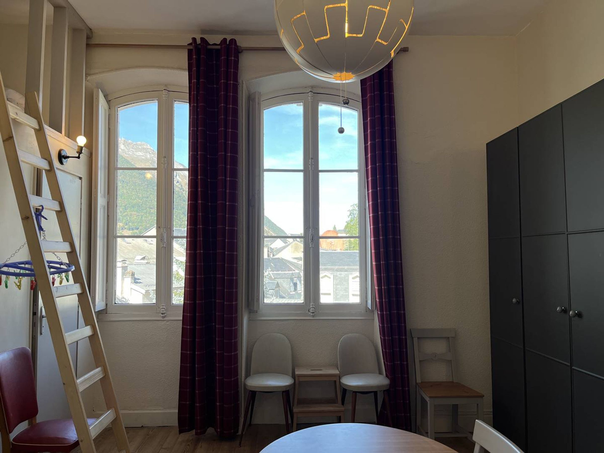 A room with a large window, two chairs, a table, a wardrobe, and a ladder.