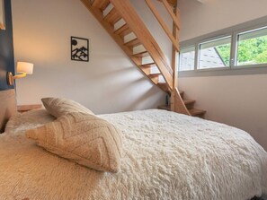 Une chambre à coucher avec un lit, des oreillers, une table de chevet, une lampe, un escalier en bois et une fenêtre donnant sur un paysage verdoyant.