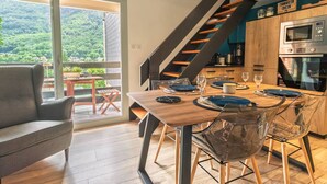 A modern kitchen with a built-in oven, a dining area with a wooden table and chairs, and a view of a forested landscape through large windows.