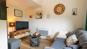 A modern living room with a sofa, a TV, a wooden TV stand, a round wall clock, and decorative items.