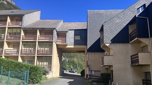 A multi-story residential building with balconies, a paved driveway, and a clear sky.
