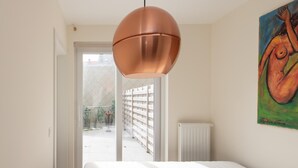 Ein Schlafzimmer mit einem weißen Bett, einer Pendelleuchte aus Kupfer und einem Bild an der Wand.