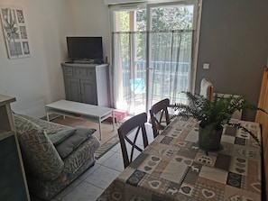 Ein Wohnzimmer mit einer Couch, einem Tisch, einem Fernseher und einer Schiebetür, die auf einen Balkon führt.