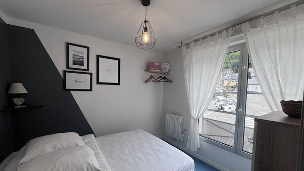Une chambre à coucher avec un lit, un radiateur, une fenêtre avec des rideaux, un luminaire suspendu et des tableaux encadrés accrochés au mur.
