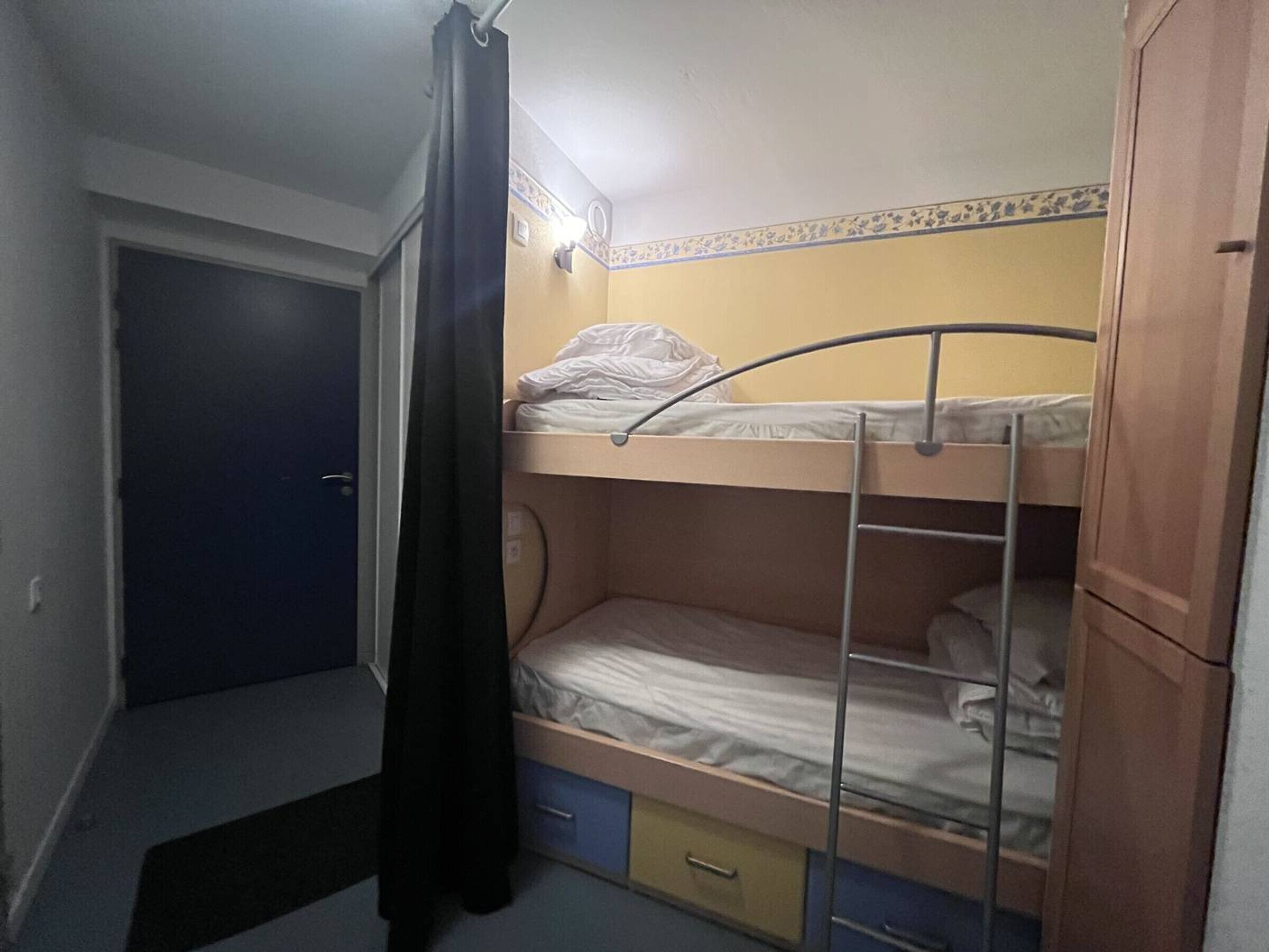 A small, compact room with a bunk bed, a single drawer, and a door.