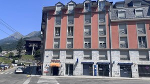 Un hôtel à plusieurs étages, avec une façade rouge, de nombreux balcons et une enseigne « Banque Populaire ».