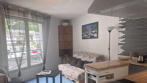 Un espace de vie compact comprenant un lit, une petite table, un bureau, une lampe et une vue sur la rue par une fenêtre.
