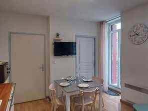 Ein Essbereich mit einem Tisch für zwei Personen, einem an der Wand befestigten Fernseher und einer Wanduhr.