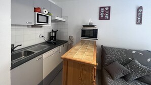 A compact kitchen with a microwave, coffee maker, and a small oven. A wooden table is placed in the center, and a sofa with patterned cushions is against the wall. - T2 for 4 people, parking, Cauterets (Cauterets)
