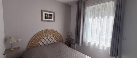 Et soveværelse med seng, natbord, lampe, et billede på væggen og et vindue med gardiner.