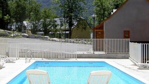 A rectangular pool with two white lounge chairs facing each other, surrounded by a white fence, with a mountain backdrop. - Studio in Cauterets with pool and pets allowed (Cauterets)