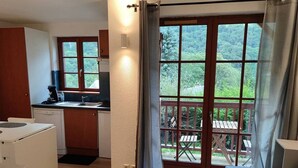 A compact kitchen with a dining area, a balcony with a table and chairs, and a view of a forested area. - Studio in Cauterets with pool and pets allowed (Cauterets)