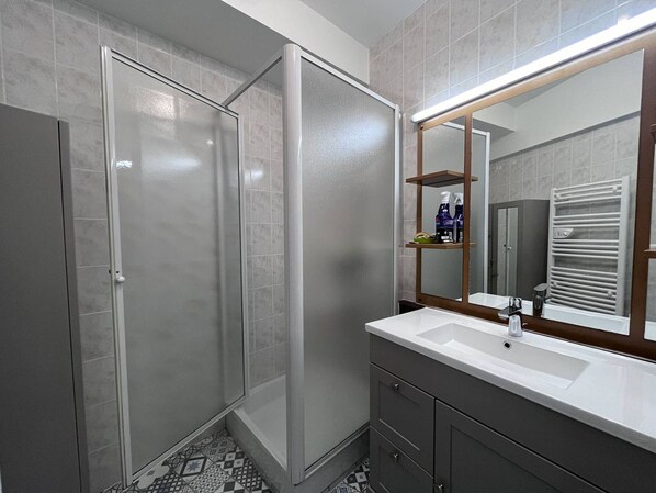 Une salle de bain moderne dotée d’une douche à l’italienne, d’un grand miroir et d’un meuble-lavabo avec un évier et un placard.