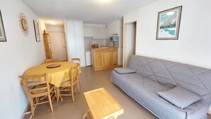 Un espace de vie compact comprenant un coin repas, une kitchenette et un canapé gris.