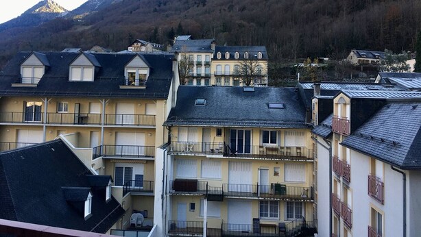 Un immeuble à plusieurs étages doté de balcons, avec une montagne en arrière-plan et un ciel dégagé.