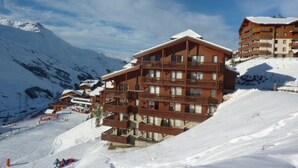 A multi-story wooden lodge with balconies, situated on a snowy mountain slope.